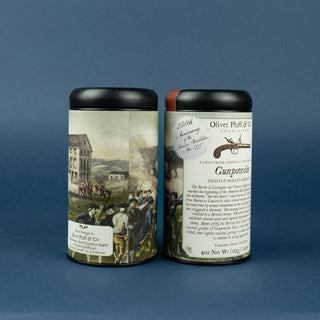 Two tins of Gunpowder tea with a label that commemorates the 250th anniversary of the Battle of Lexington and Concord on a blue background