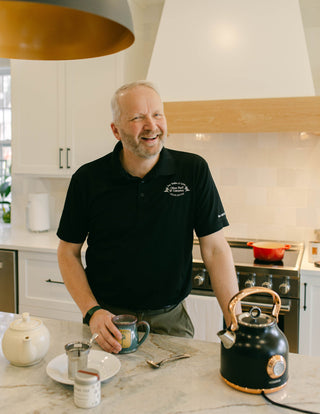 photo of white man in black shirt at kitchen counter drinking tea