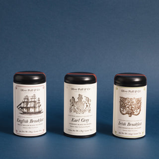 three black tea tins with black and white graphics of sailing ship, early American people and flowery design against a blue background