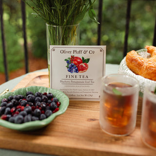 blueberry pomegranate iced tea envelope on a tray, outdoors, next to a bowl of pomegranates and blueberries