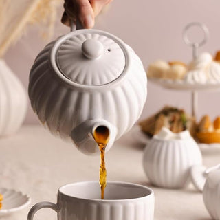 white teapot pouring hot tea into white teacup
