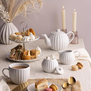 white teapot, teacup, milk jug, and sugar bowl on table setting with pastries and utensils.