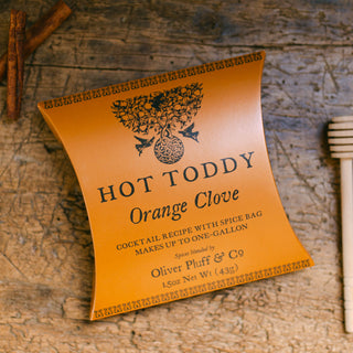 Hot Toddy Orange Clove cocktail recipe label on a wooden surface with cinnamon sticks and a honey dipper.
