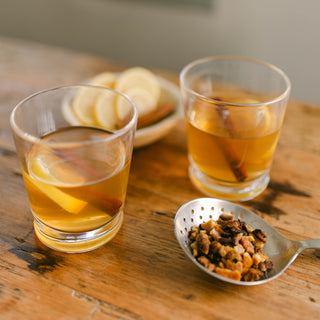 Two glasses of hot toddy with a spoonful of spices on a wooden table.