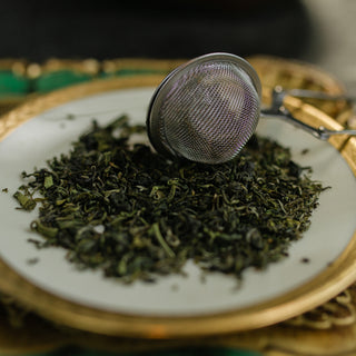Tea strainer on a plate with dried green tea leaves