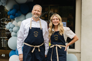 photo of a man and woman wearing aprons standing in front of the exterior of the tea shop