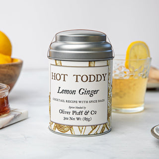 small silver tea tin with yellow flowery design in front of bowl of yellow lemons and glass of tea