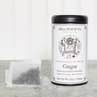 black tea tin with white tea bag beside it standing on white counter