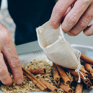 two man hands putting cinnamon sticks and loose leaf tea in white mesh tea bag