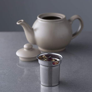 beige tea pot and stainless steel tea cut filter on marble counter