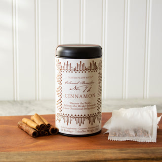 black tea tin with orange pattern on label sitting beside pile of cinnamon sticks and white mesh tea bags