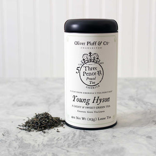4oz loose tea, sealed in matte black signature tea tin beside small pile of green tea leaves on kitchen counter