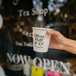 person's hand holding cup of tea in front of store window