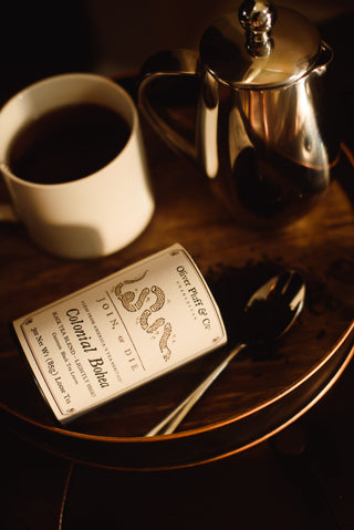 colonial bohea tea tin open on tabletop with tea spilling out
