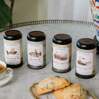 four tea tins on marble tray surrounded by pastries