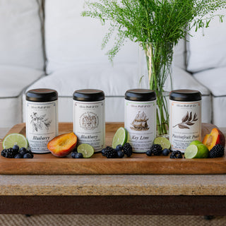 four tea tins sitting on wooden tray surrounded by fresh fruits