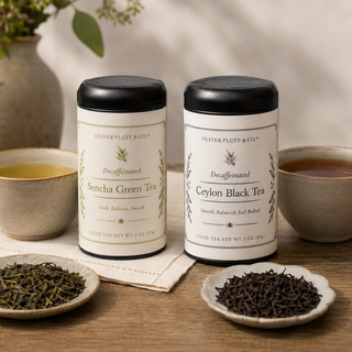 two tea tins sitting on wooden tabletop with loose green tea and black tea sitting in front in small ceramic bowls