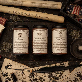 photo of three commemorative tins on tabletop surrounded by loose tea and a candle