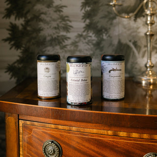 Three cylindrical tea containers with labels on a wooden surface with a decorative background