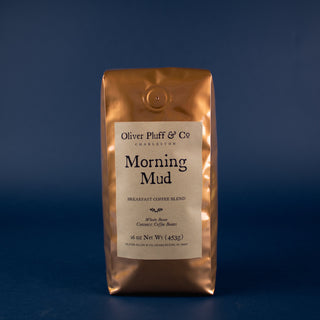 orange shiny coffee bag with brown label sitting on blue back drop. Morning mud whole bean