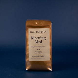 orange shiny coffee bag with brown label sitting on blue back drop. Morning mud ground