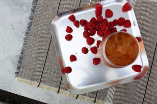 glass of iced tea with red raspberries sprinkled beside it on a silver platter