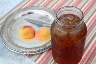 large glass mason jar filled with iced peach tea, sitting beside 3 peaches outside