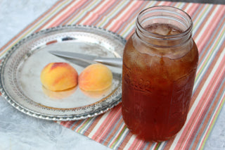 large glass mason jar filled with iced peach tea, sitting beside 3 peaches outside