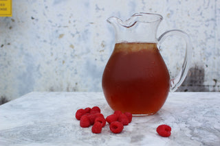 glass pitcher of iced tea with red raspberries sprinkled beside it on a silver platter