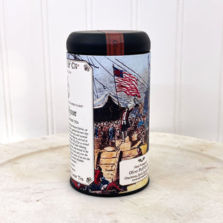 side view of black tea tin with graphic from boston tea party on white plate