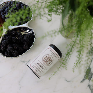 Blackberry product on a marble surface with a bowl of blackberries and greenery.