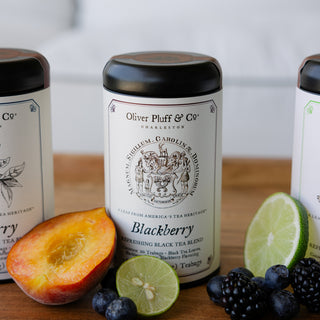 Tea canisters with fruit and tea leaves on a wooden surface, featuring Oliver Pluff & Co branding.