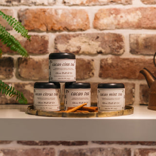 4 tins of cacao tea next to copper kettle on shelf