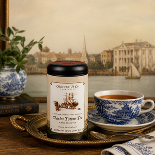 charles towne tea tin on brass tray in front of a painting sitting next to filled teacup