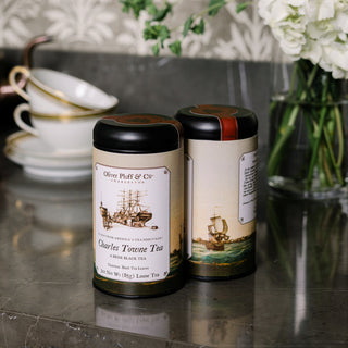 Two tea canisters with ship illustrations on labels on a reflective surface.