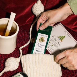 green foil bag of christmas coffee being added by hand to a cream stocking on a red blanket