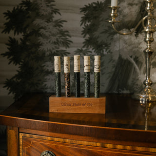labelled tubes filled with 5 different teas in wood block that reads 'oliver pluff' on top of an ornate wood furniture piece with silver candlestick in background