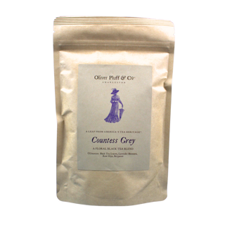 shiny silver tea pouch bag with old timey woman with a hat and umbrella on label against a blue backdrop