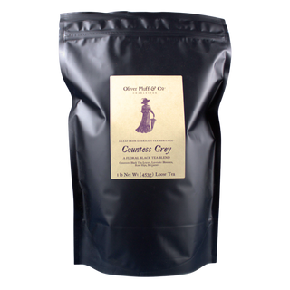 shiny black tea pouch bag with old timey woman with a hat and umbrella on label against a blue backdrop