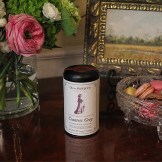 Tea canister labeled 'Countess Grey' on a table with flowers and a painting in the background