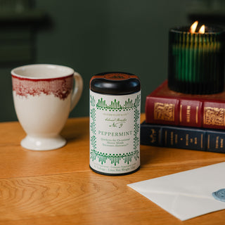 peppermint tea tin with white label and black lid, sitting on wooden tabletop with a green candle sitting on top of two books in the background