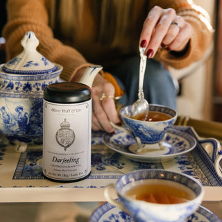 Person enjoying a cup of tea with a Darjeeling tea canister on a table.