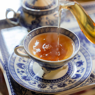 Tea being poured into a blue and white teacup on a matching saucer.