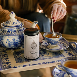 Tea canister with a tea bag, teacup, and saucer on a decorative table.