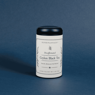 A cylindrical white tin of Oliver Pluff & Co. Decaffeinated Ceylon Black Tea with a black lid, set against a dark blue textured background.