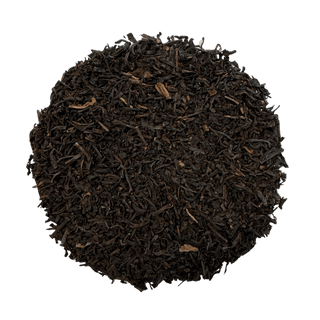 A circular pile of dark brown loose-leaf tea leaves on a solid green background.