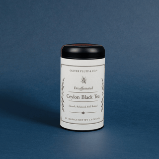 A cylindrical tin of Oliver Pluff & Co. Decaffeinated Ceylon Black Tea, featuring a white label and black lid, set against a solid dark blue background.