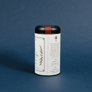 A white cylindrical tea tin with a black lid and a thin red band, standing on a dark blue background. The label features elegant black botanical illustrations and text.