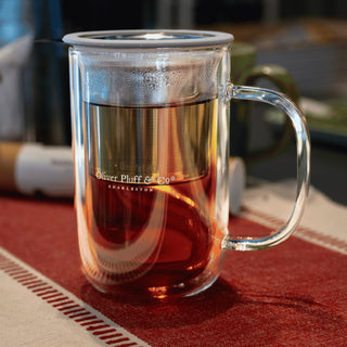 clear glass mug that reads 'oliver pluff & co' with stainless steel brewing basket filled with water and steeping tea