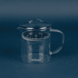 Clear glass tea infuser with black lid on a dark blue background